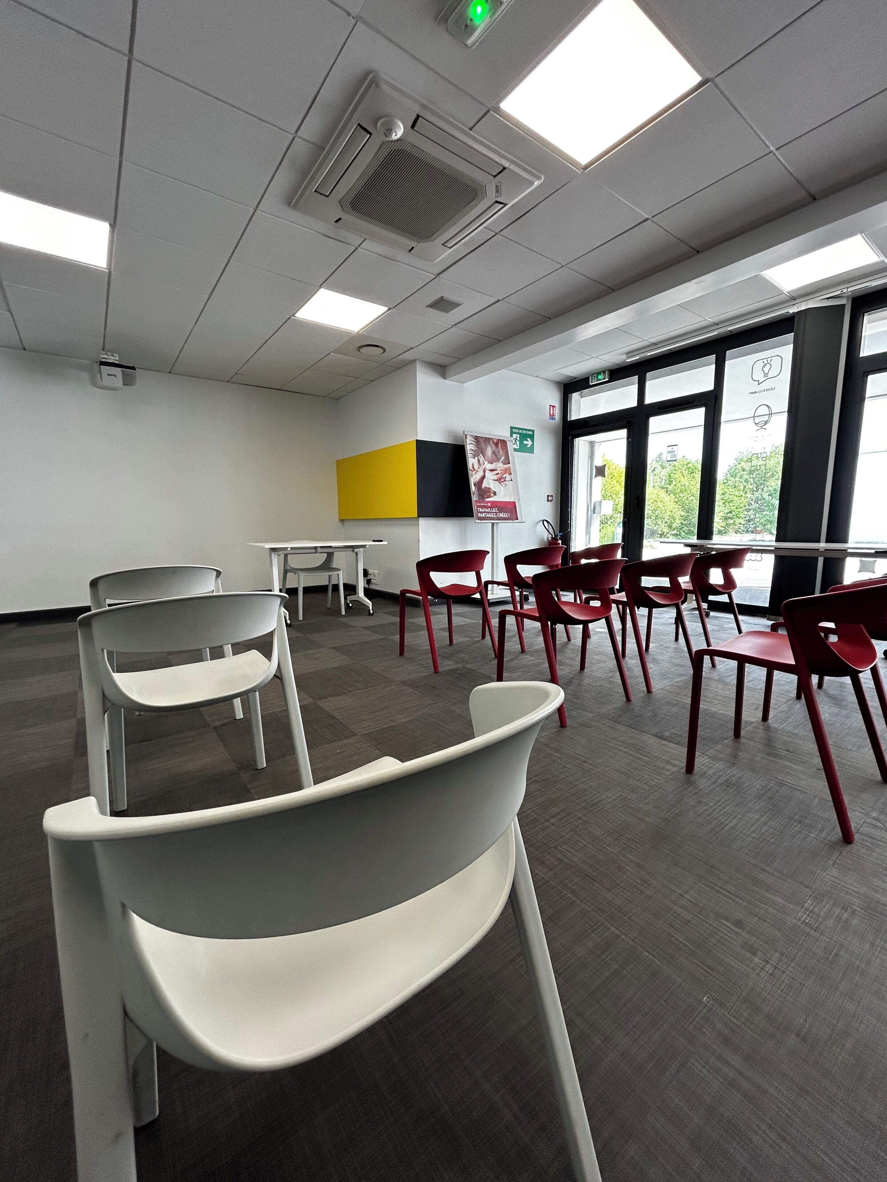 Un salón de conferencias con sillas blancas y rojas, una mesa blanca y ventanas amplias.