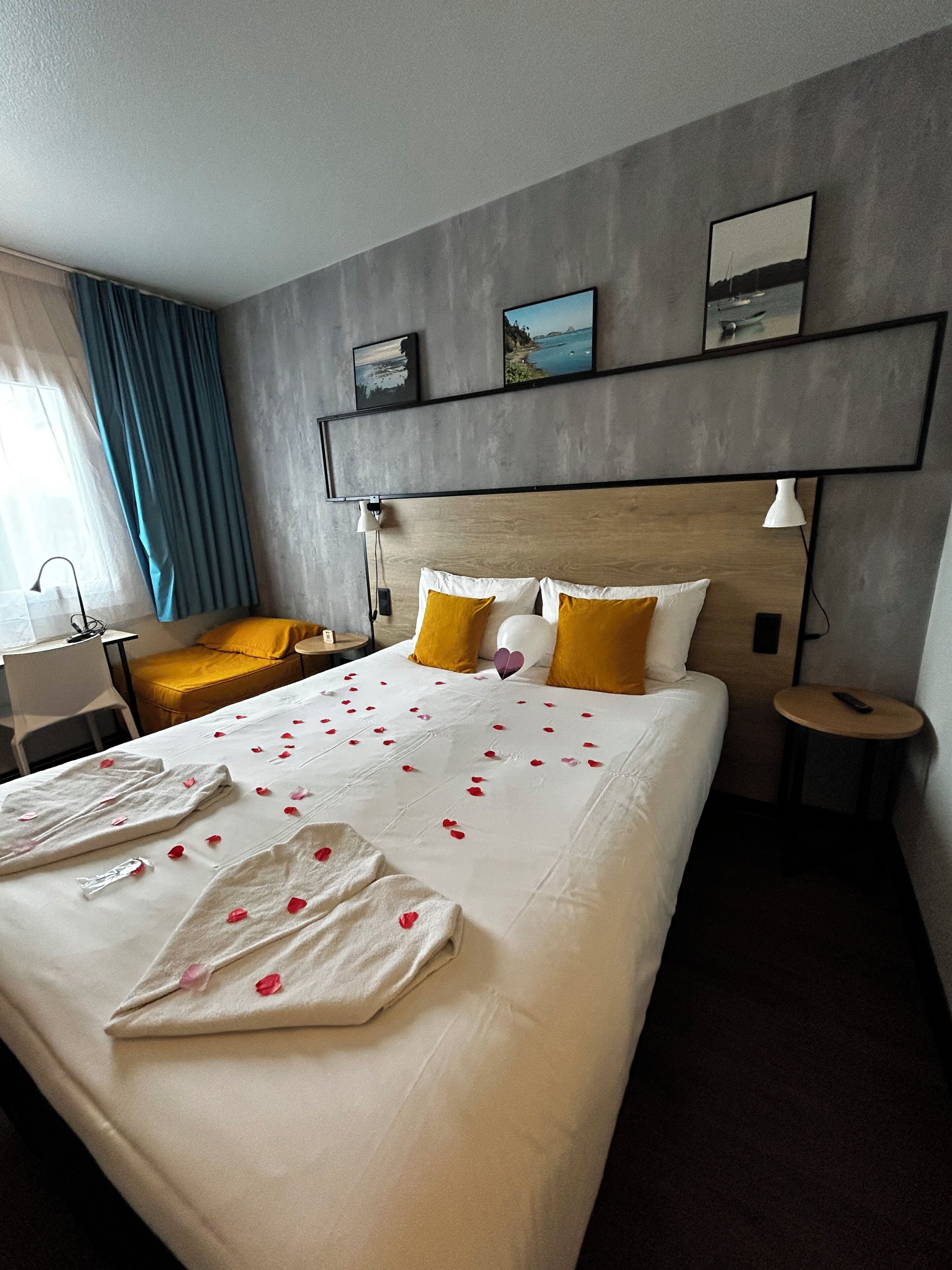 Ein Hotelzimmer mit Bett, Nachttischen, einer Lampe, einem Sessel, einem Schreibtisch und einem Fenster mit Vorhängen.