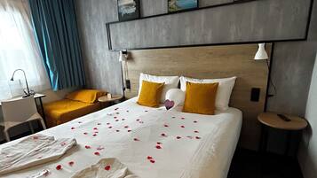 Ein Hotelzimmer mit Bett, Nachttischen, einer Lampe, einem Sessel, einem Schreibtisch und einem Fenster mit Vorhängen.