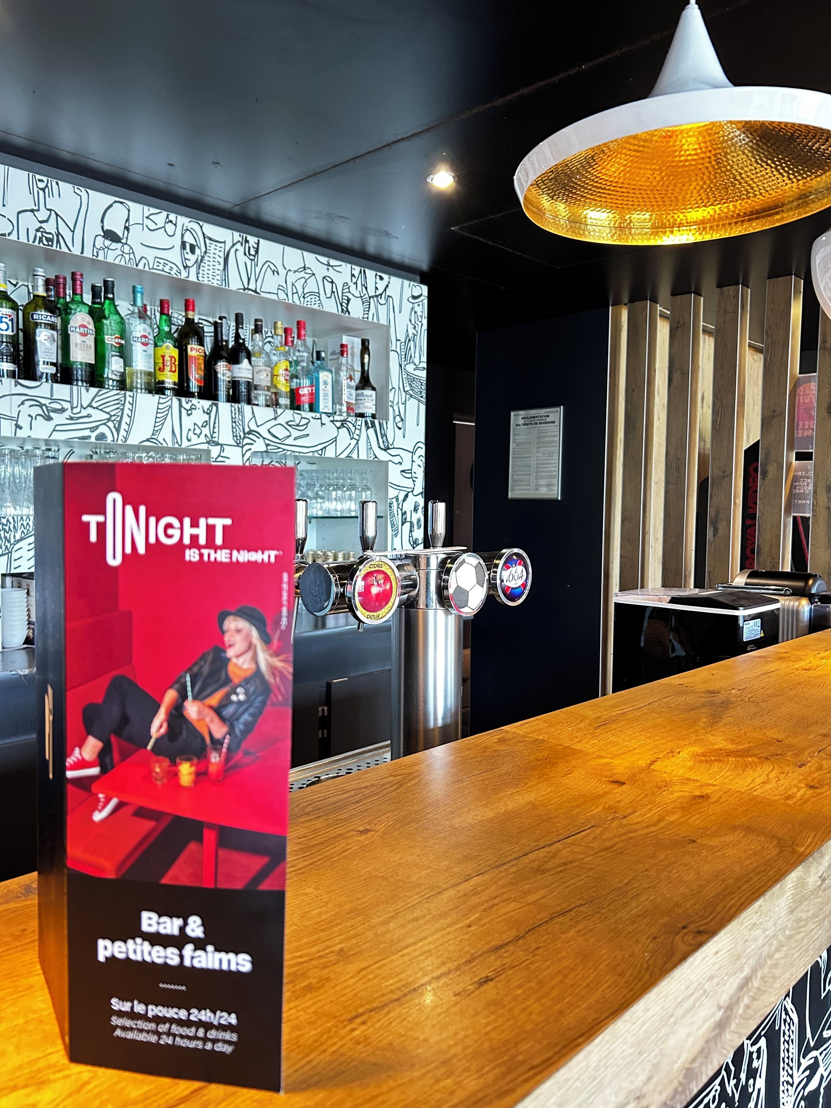 A bar area with a red sign, a variety of liquor bottles, and a modern light fixture.
