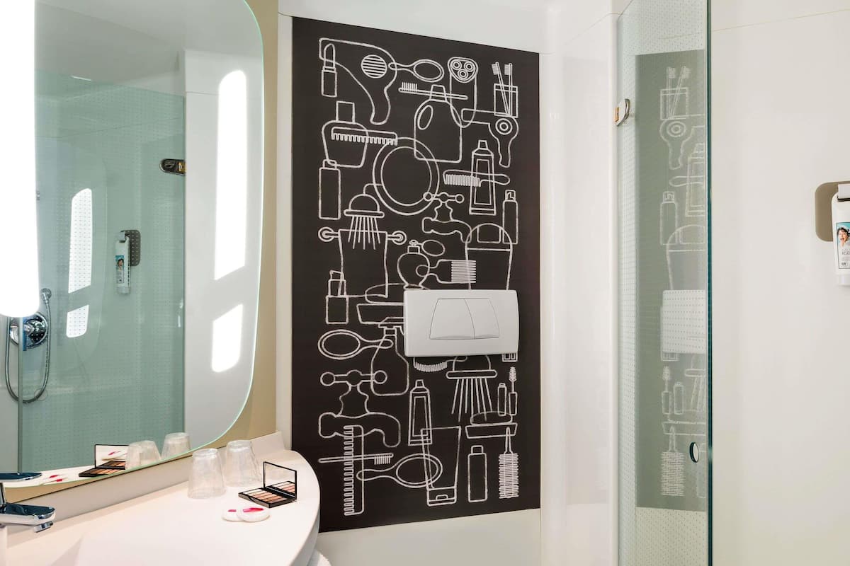 A bathroom with a large mirror, a sink with toiletries, and a shower area.