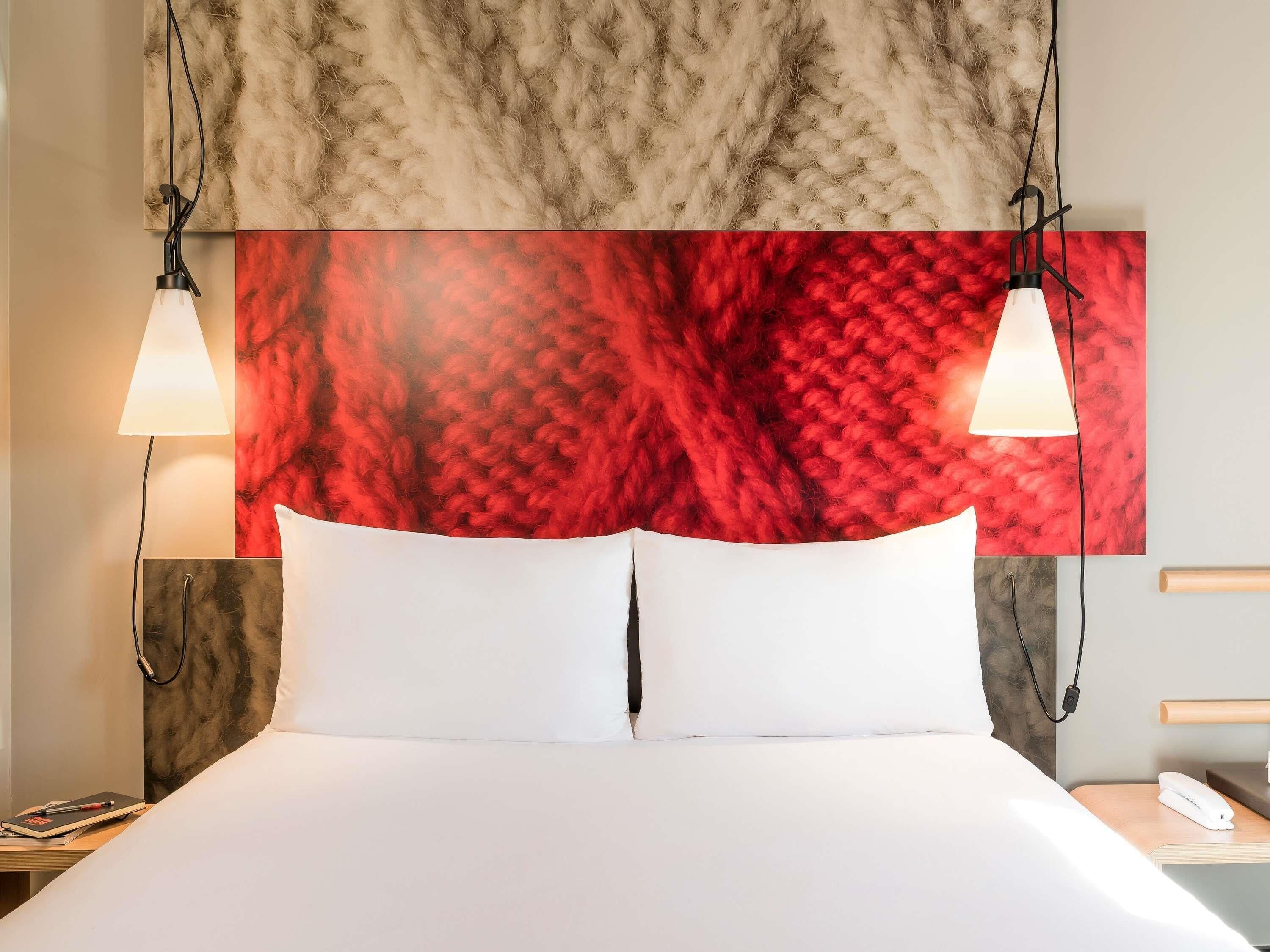 Een hotelkamer met een groot bed, twee bedlampen, een rode structuurwand en een houten hoofdeinde.