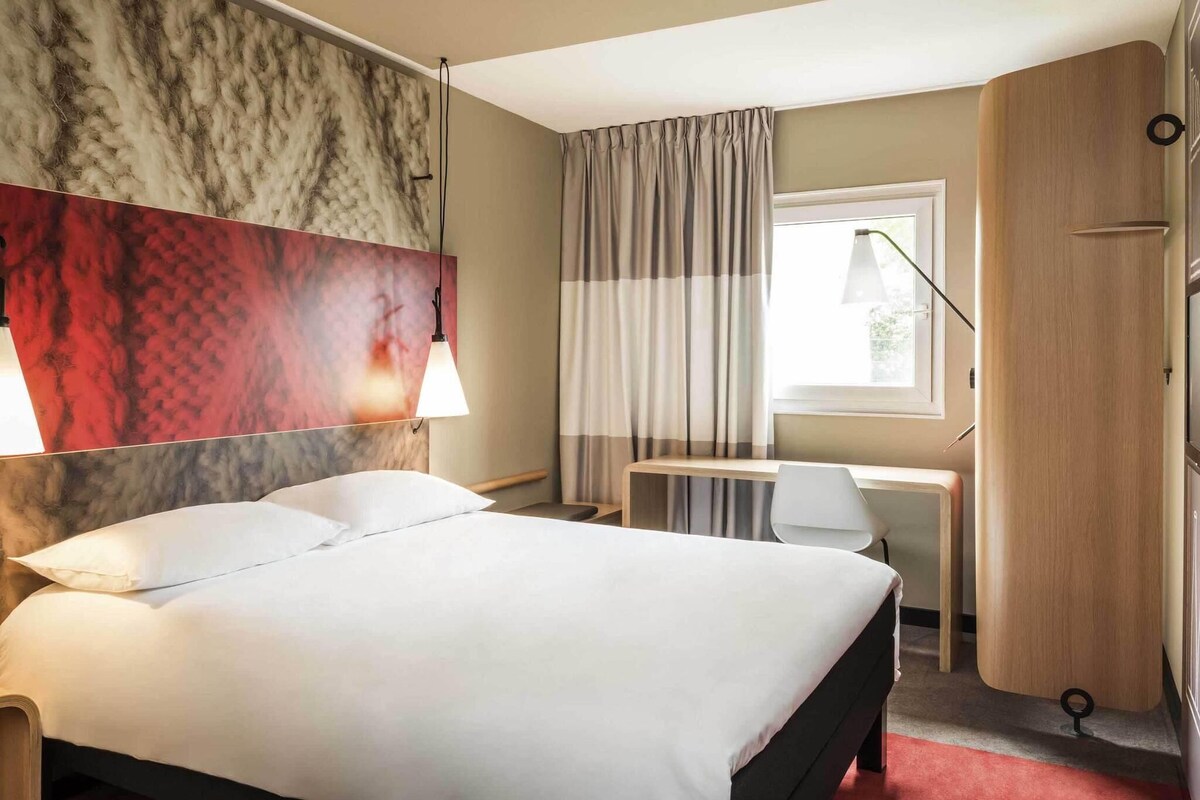 A hotel room with a bed, desk, chair, and wardrobe.
