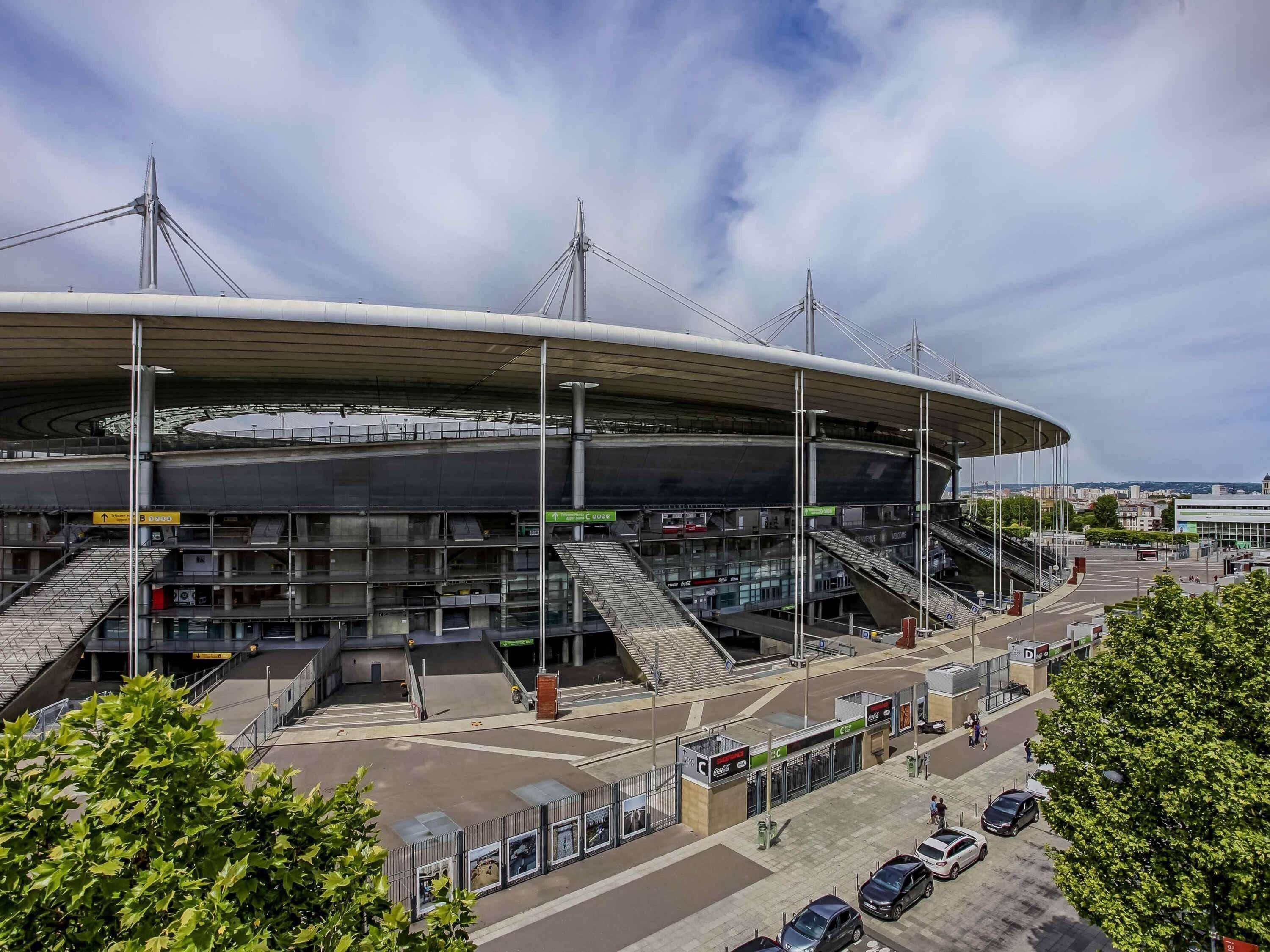 En arena med flera våningar av sittplatser, en överbyggd entré och en parkeringsplats med bilar.