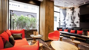 Un salon moderne avec des canapés rouges, des tables en bois et une grande fenêtre donnant sur un paysage urbain.