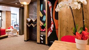 Un espace d’accueil moderne avec un comptoir de réception en bois, des sièges rouges et une grande affiche représentant une canette de soda.