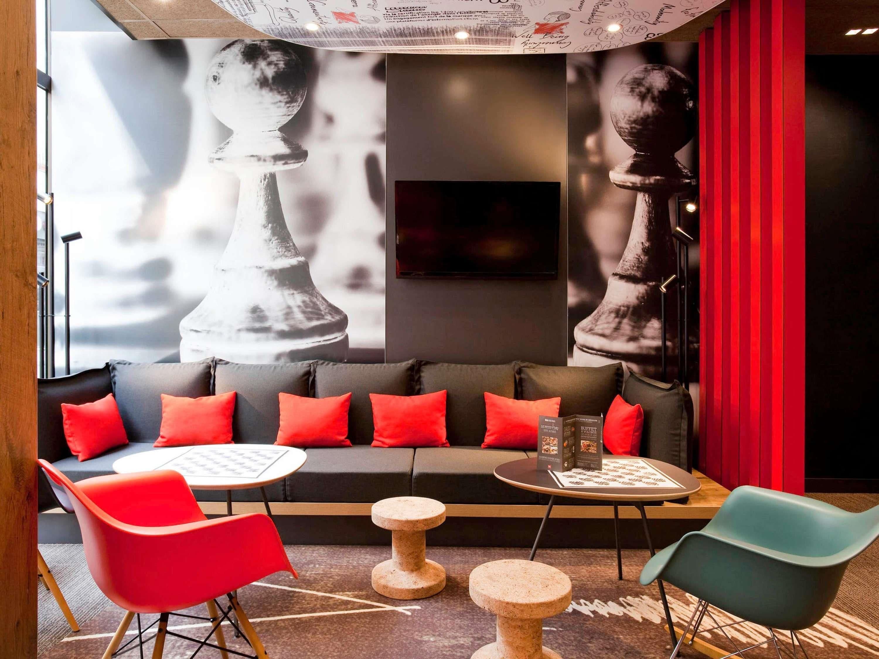 Un espace détente moderne comprenant un canapé, des fauteuils rouges et bleus, une table basse et un jeu d’échecs.