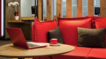 Um interior moderno com uma mesa de madeira redonda, assentos em vermelho e cinza, um laptop e uma caneca vermelha.