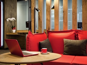 Un interior moderno con una mesa redonda de madera, asientos rojos y grises, una computadora portátil y una taza roja.