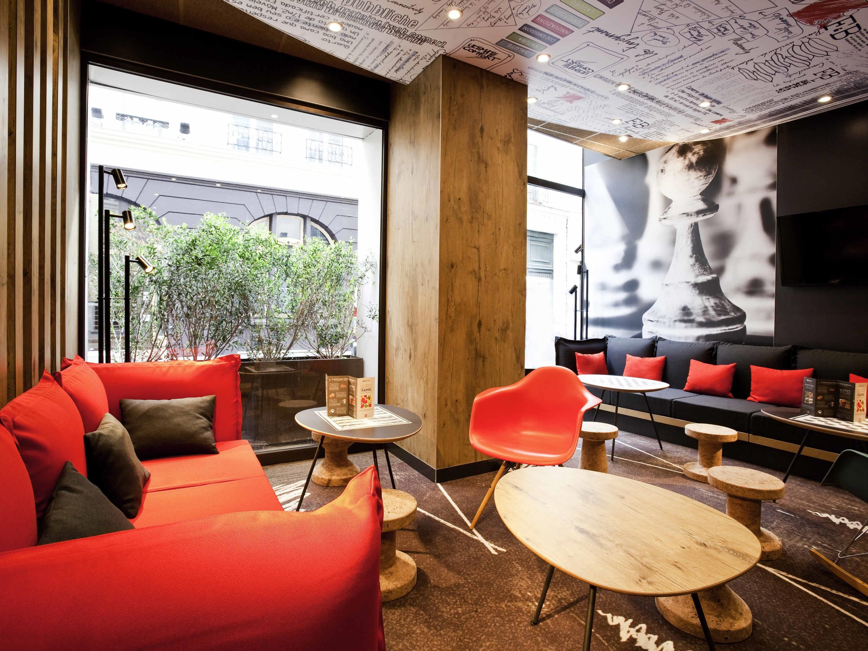 Een modern interieur met een rode bank, houten tafels en een groot raam met uitzicht op een straat.