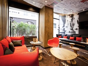 Un intérieur moderne avec un canapé rouge, des tables en bois et une grande fenêtre donnant sur une rue.