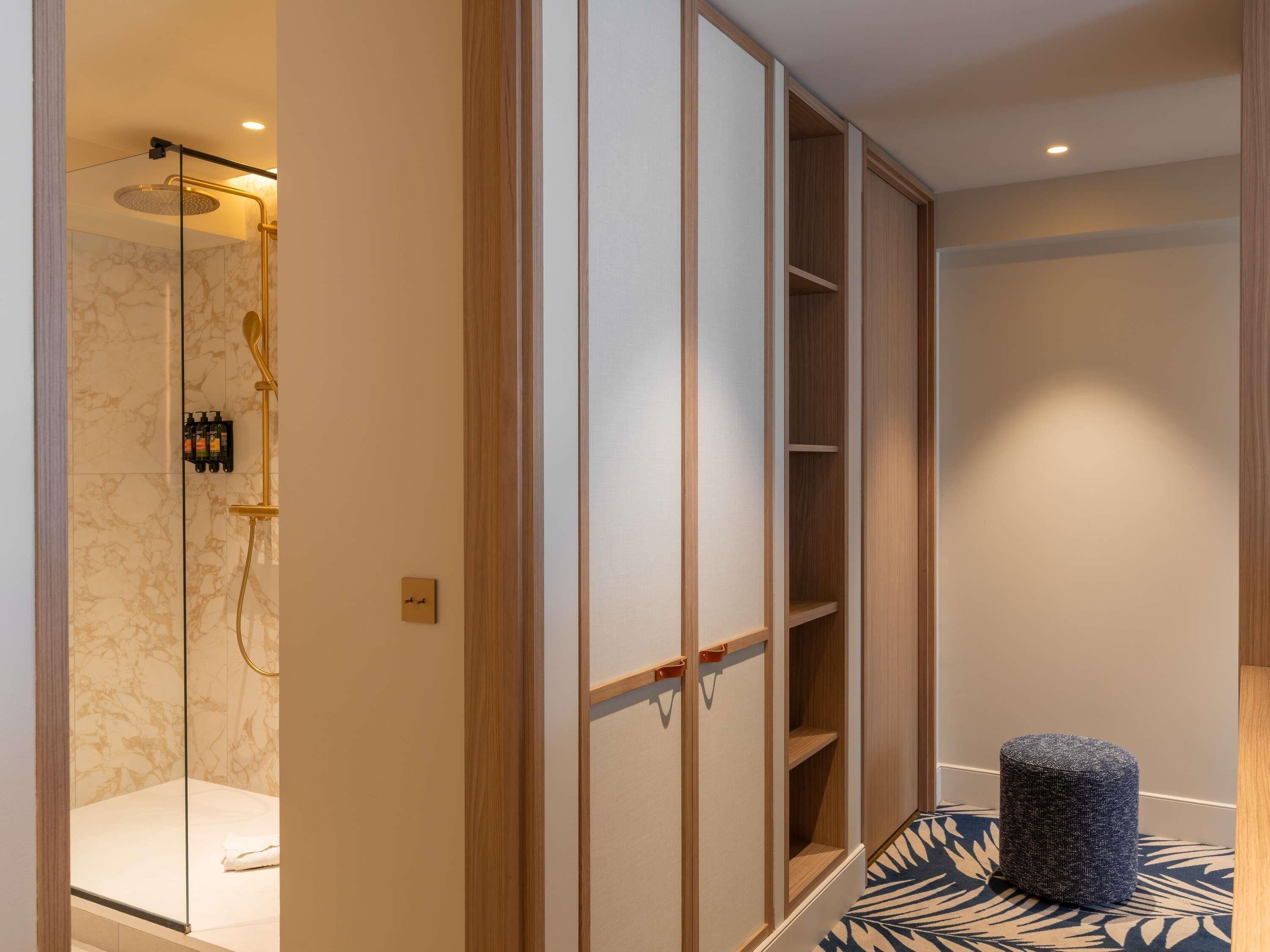 A modern bathroom with a glass-enclosed shower, wooden shelving, and a patterned floor.