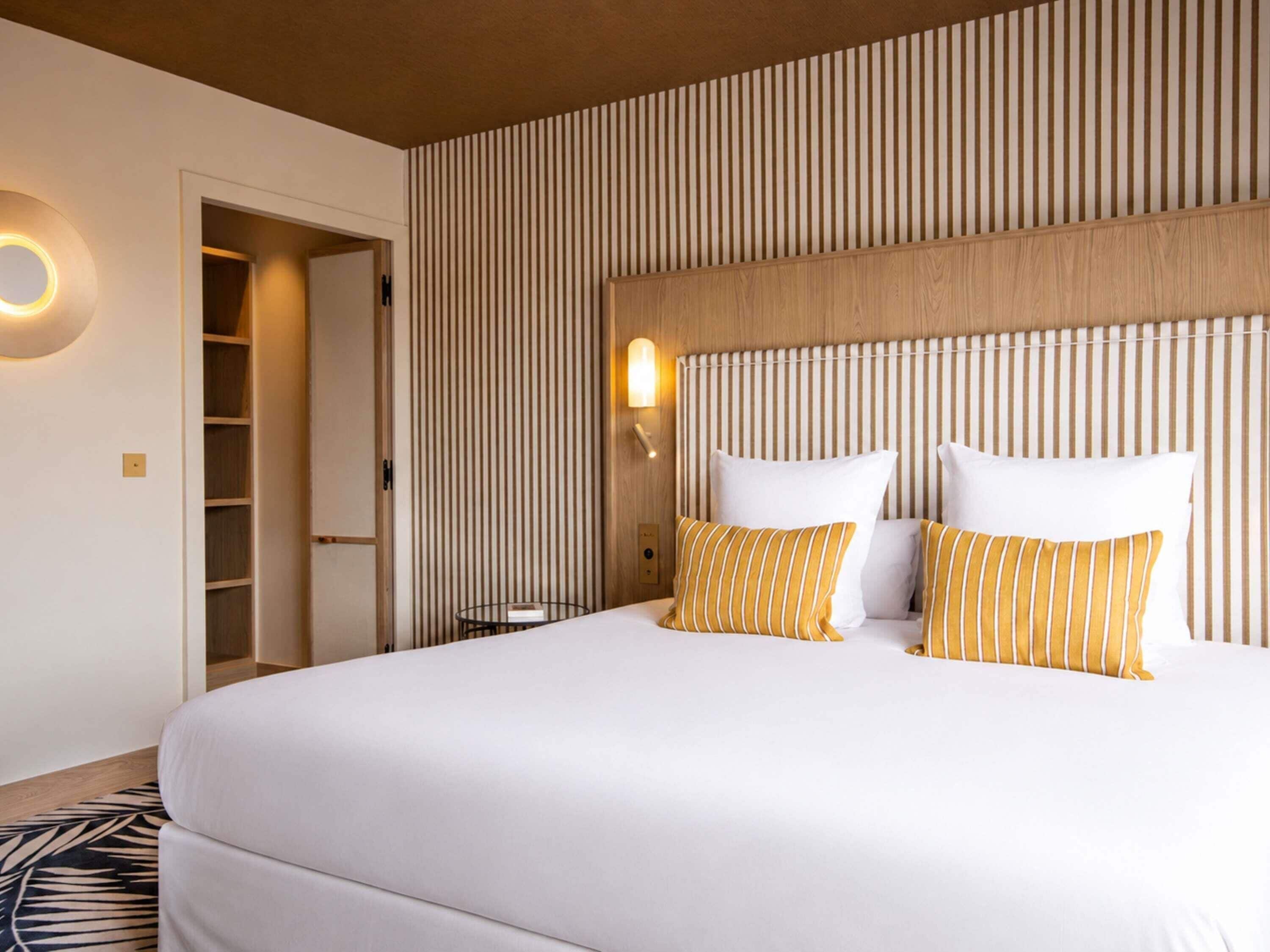 Una habitación de hotel con una cama grande, un cabecero de madera, una mesita de noche, una lámpara y un armario.