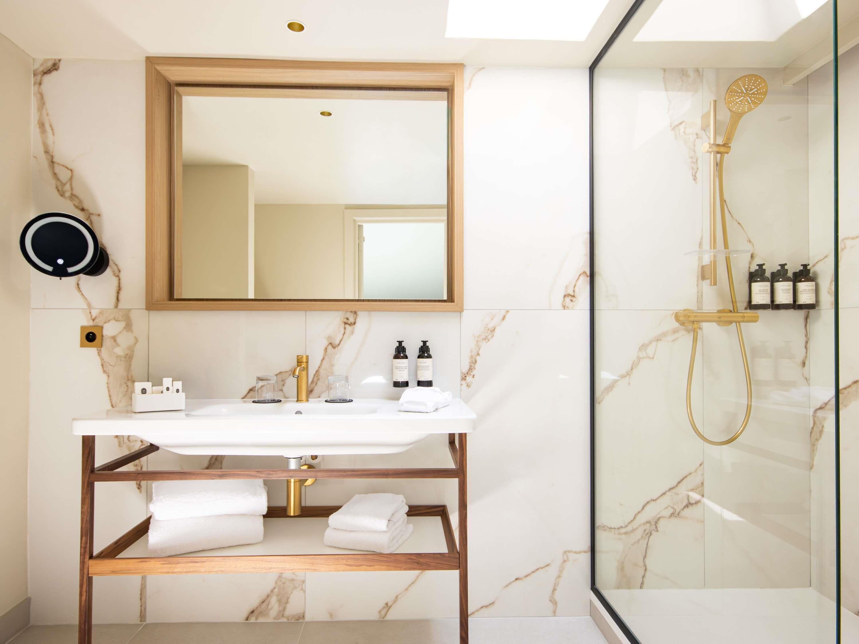 Ein Badezimmer mit Marmorwaschtisch, Brausekopf aus Gold und einer Glasdusche.