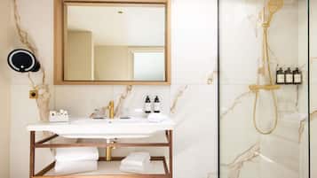 Ein Badezimmer mit Marmorwaschtisch, Brausekopf aus Gold und einer Glasdusche.