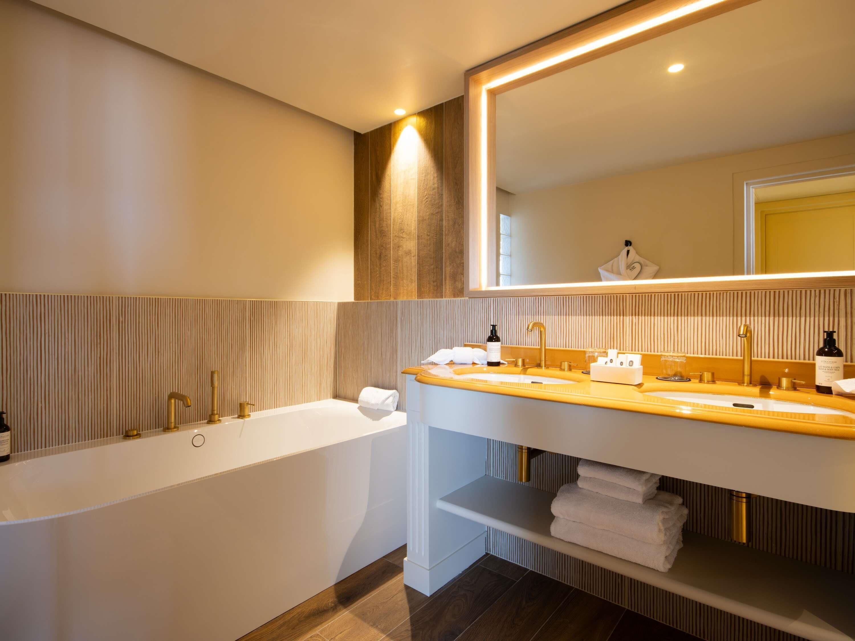 A modern bathroom with a bathtub, a vanity with a mirror, and a shelf with towels.