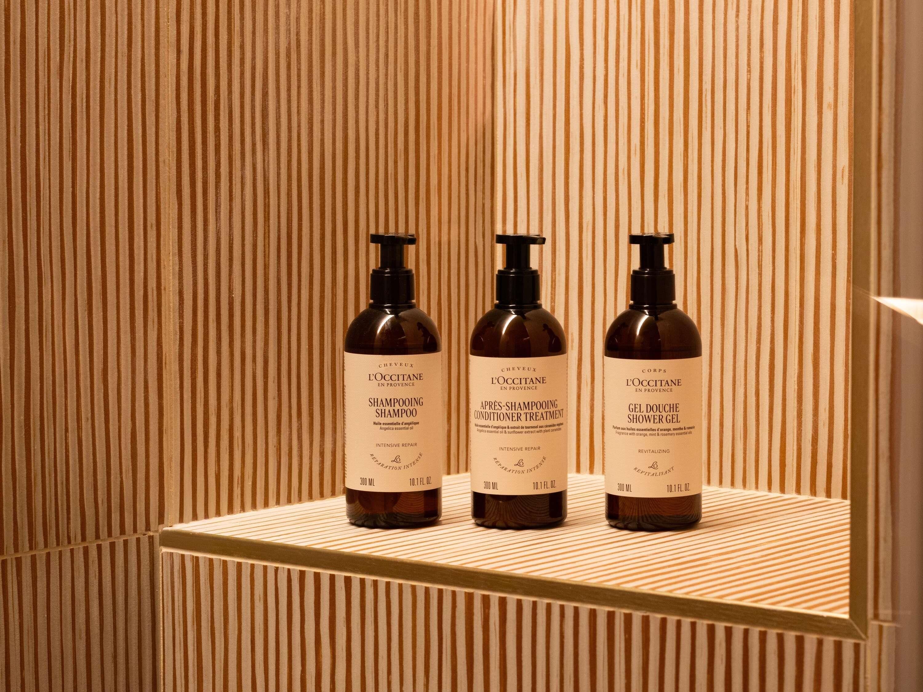 Three bottles of shampoo, conditioner, and shower gel on a wooden shelf.