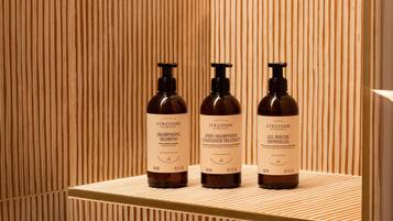 Three bottles of shampoo, conditioner, and shower gel on a wooden shelf.