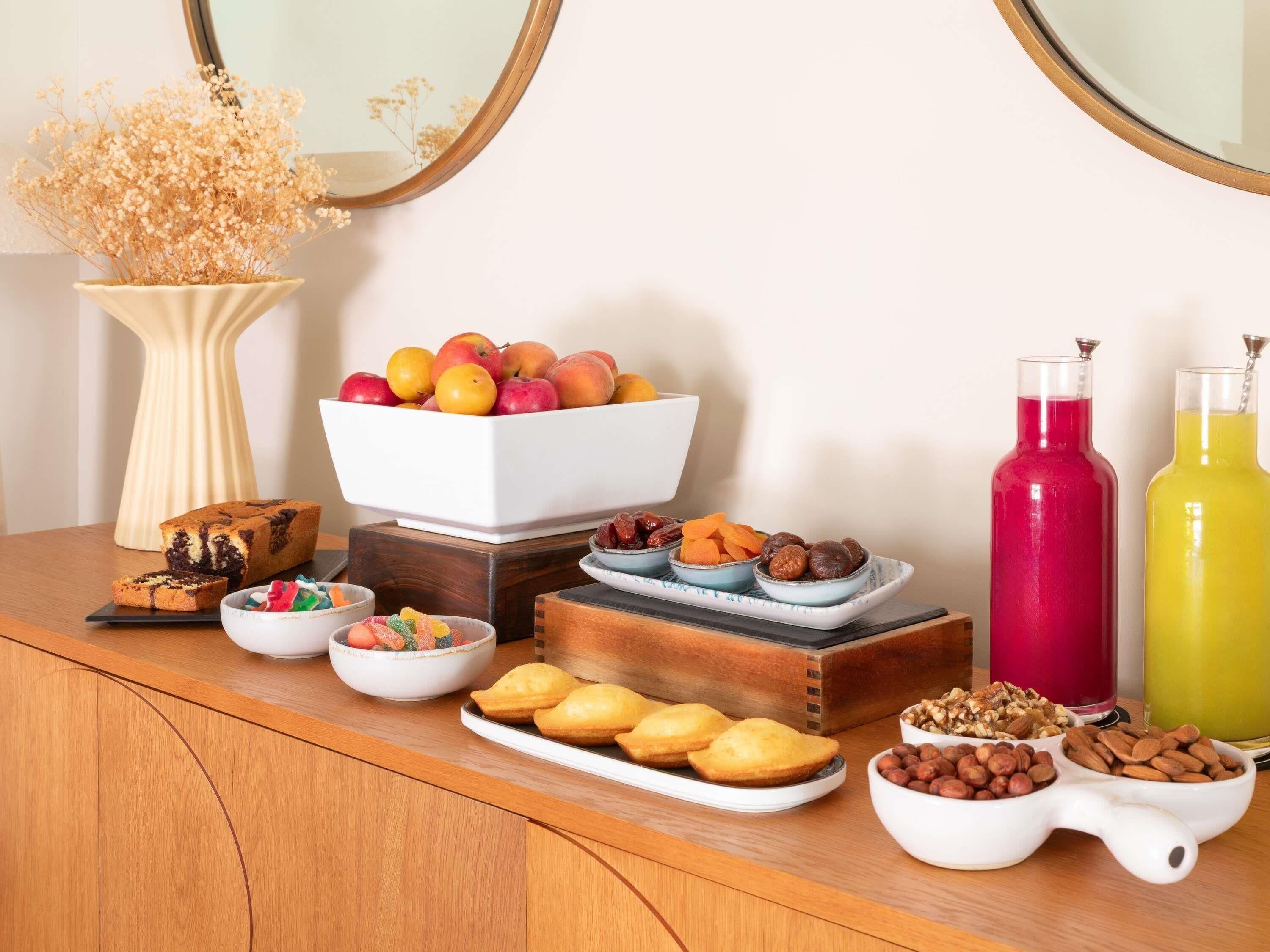 A wooden table with various food items, including a bowl of apples, a plate of pastries, and a bowl of nuts.