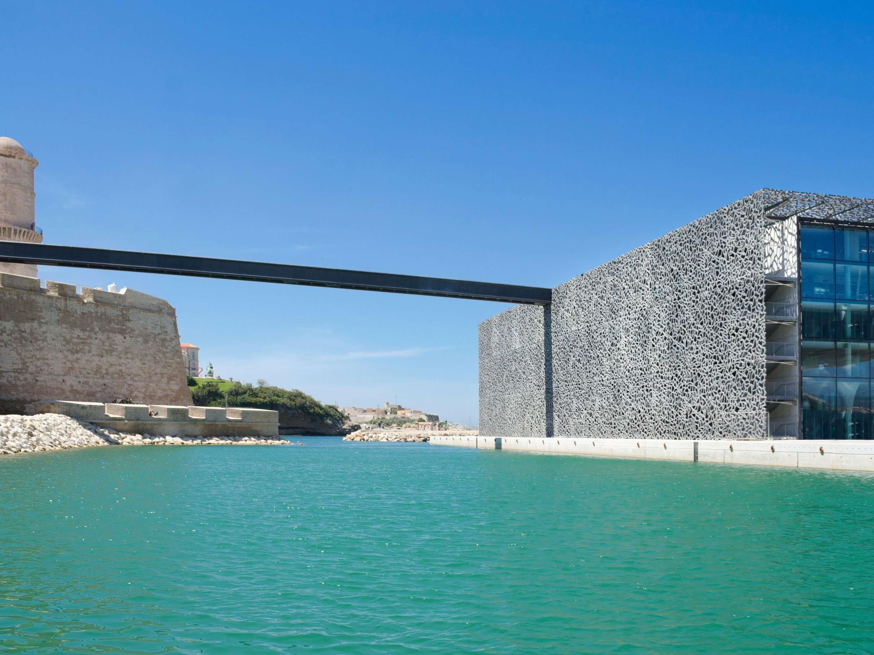 A coastal view with a bridge, a historic fort, and a modern building with a textured facade.