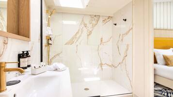 Un baño moderno con ducha de mármol blanco, grifo dorado y lavamanos blanco.
