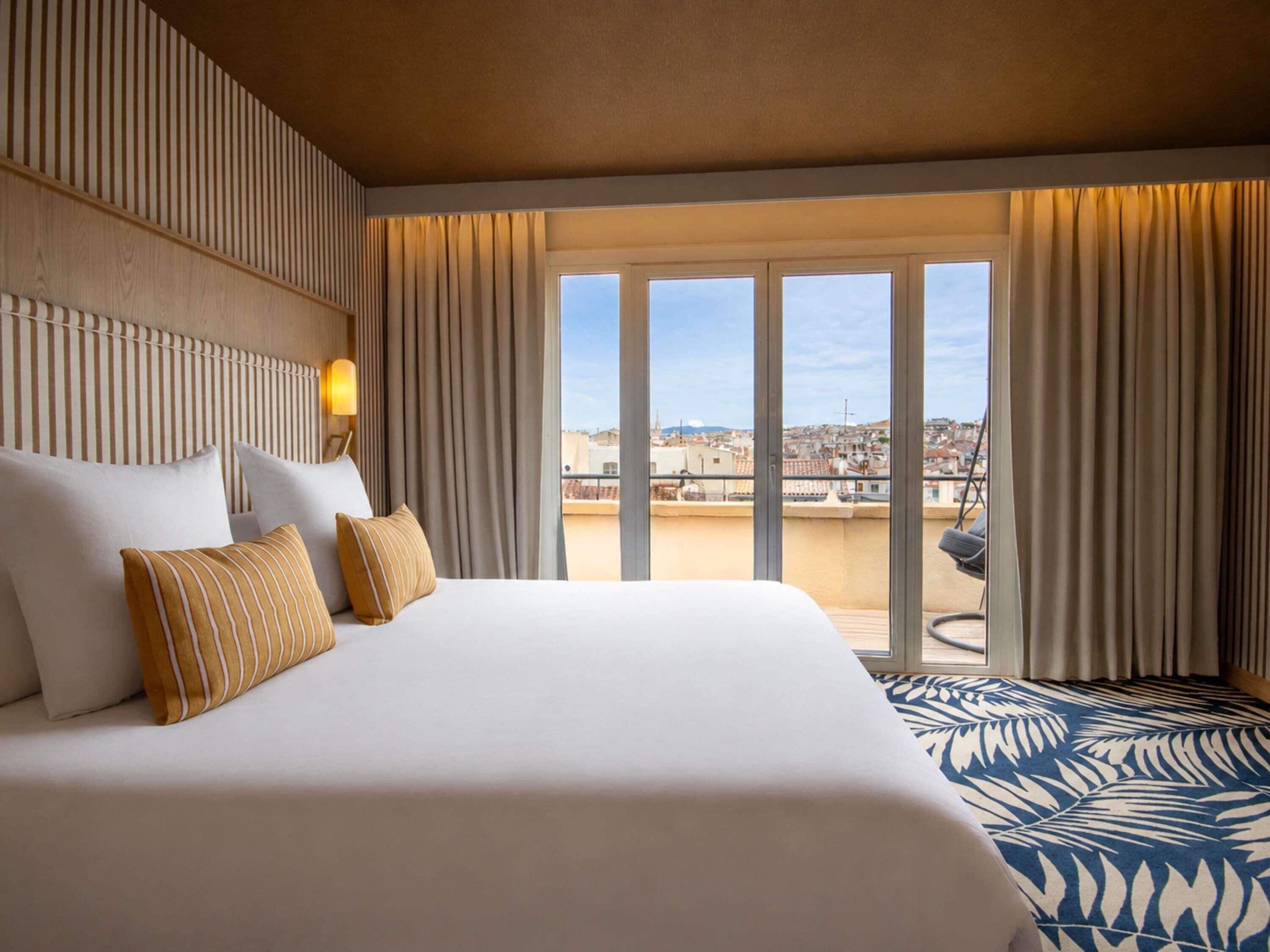 Habitación de hotel con una cama grande, vistas de la ciudad y un balcón.