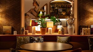 A cozy bar area with a wooden herringbone wall, a large mirror reflecting the bar, and a variety of plants and candles on the counter. - Grand Hotel Beauvau Marseille Vieux-Port - MGallery Collection (Marseille)