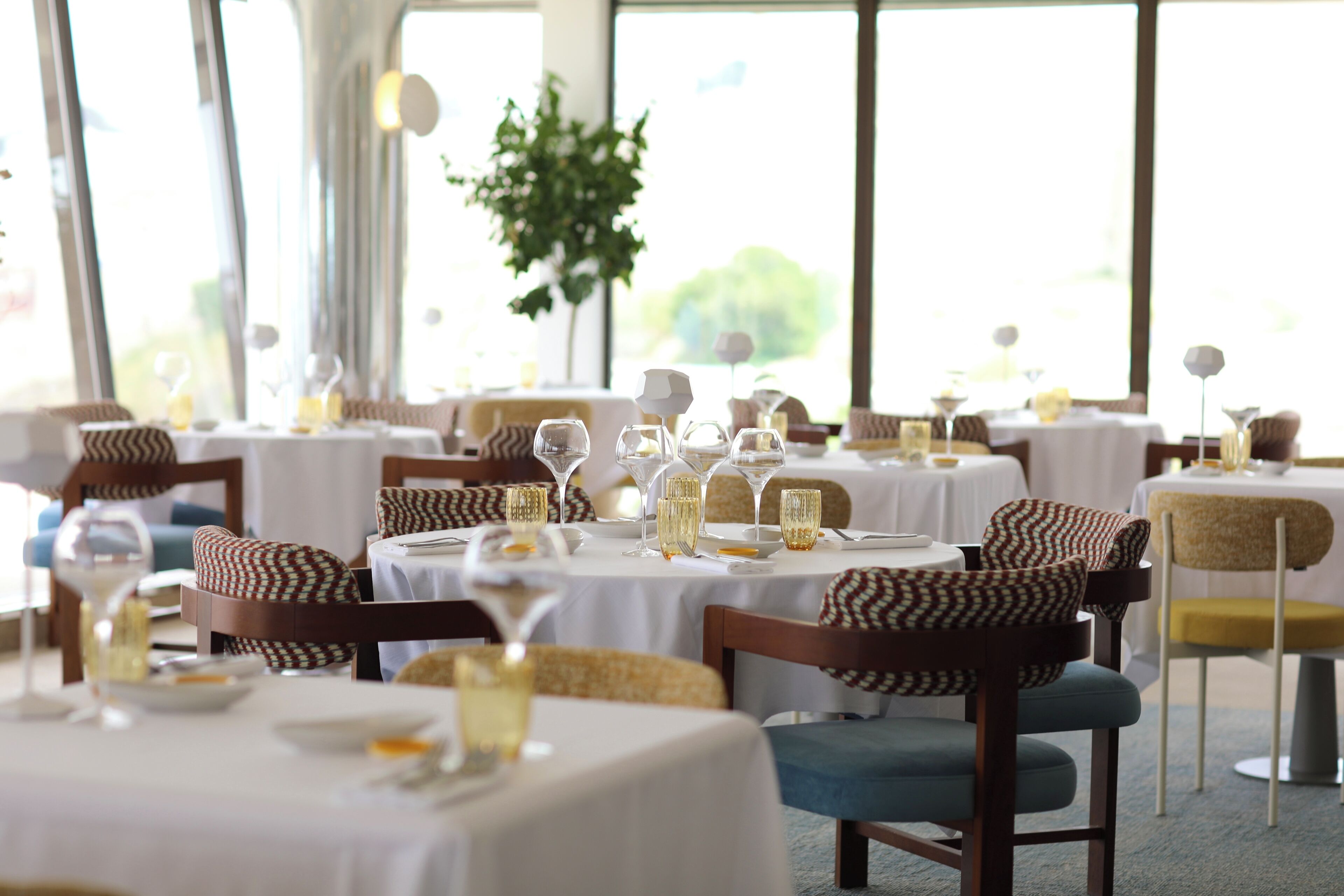 A restaurant with round tables set for dining, featuring white tablecloths and glassware.
