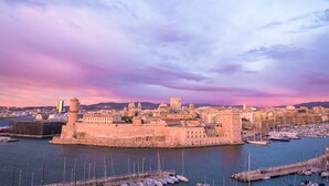 A coastal cityscape with a prominent fortress-like structure surrounded by water, a marina with boats, and a backdrop of buildings and hills. - Sofitel Marseille Vieux Port (Marseille)