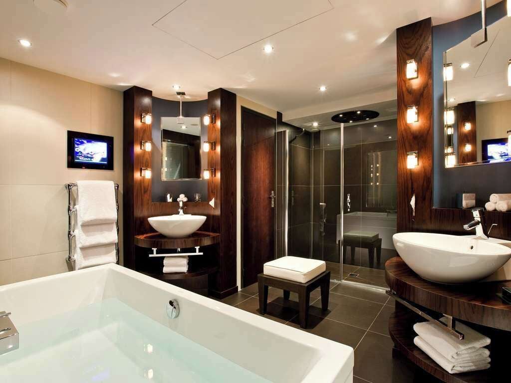 A modern bathroom with a large bathtub, two sinks, a shower, and a television.