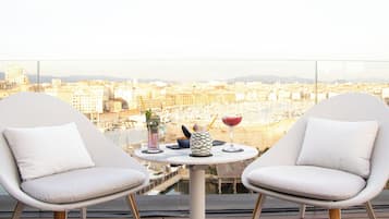 En balkon med to hvide stole, et lille rundt bord og udsigt over byen.