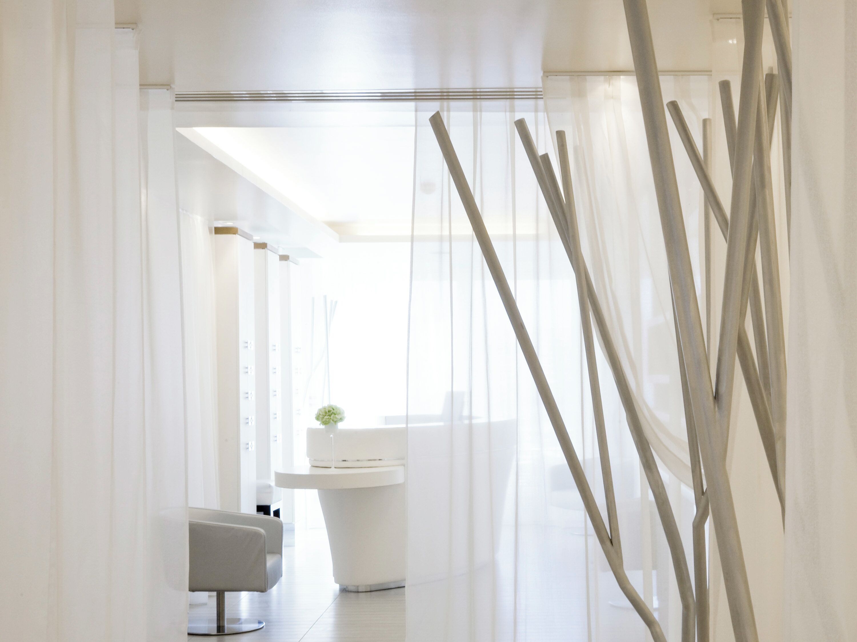 A modern, minimalist bathroom with a white sink, a chair, and a decorative plant.