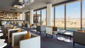A modern bar with a city view, featuring seating areas with cushioned chairs and round tables. - Sofitel Marseille Vieux Port (Marseille)