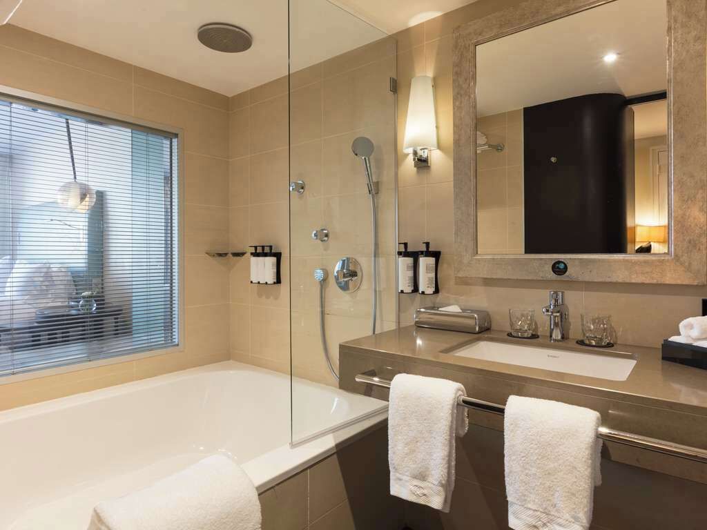 A modern bathroom with a glass-enclosed shower, a large mirror, and a bathtub.