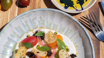 A wooden table with a plate of food, a bowl of olive oil, and a variety of colorful tomatoes.