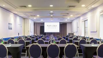 Une salle de conférence avec des rangées de tables et de chaises, un écran de projection affichant le texte « SOFITEL HOTELS & RESORTS MARSEILLE VIEUX PORT », et des bouteilles d’eau posées sur les tables.