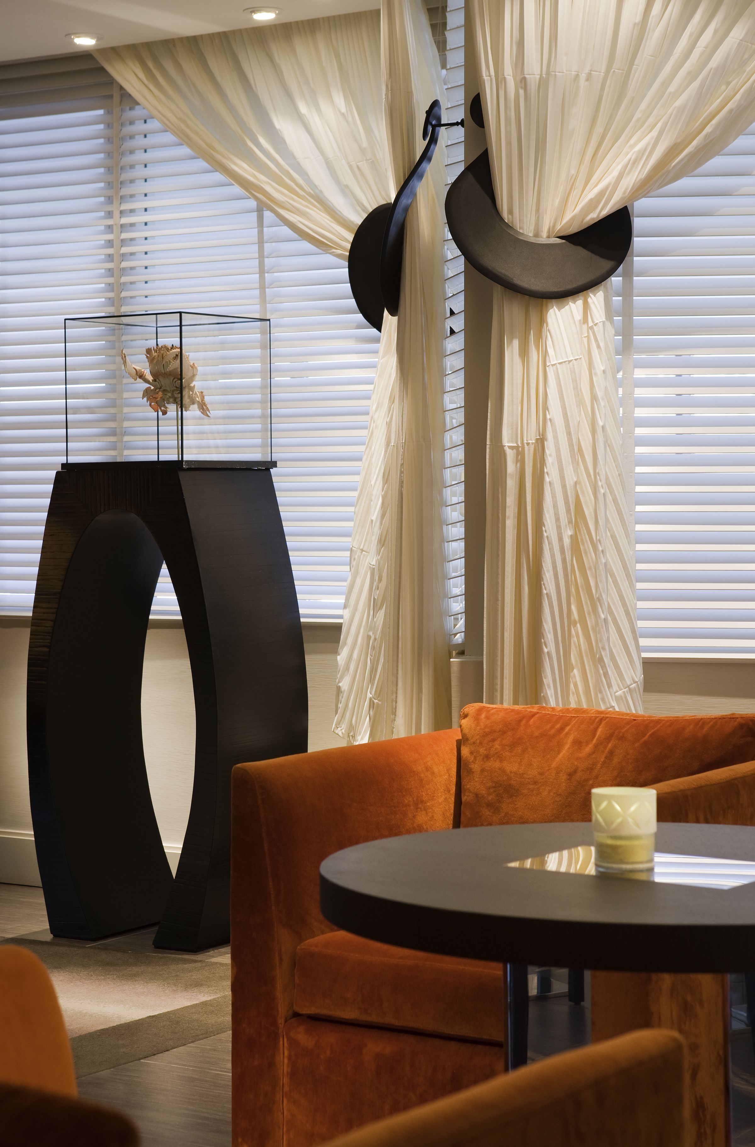 A modern interior with a round table, orange upholstered seating, and a unique black sculpture.