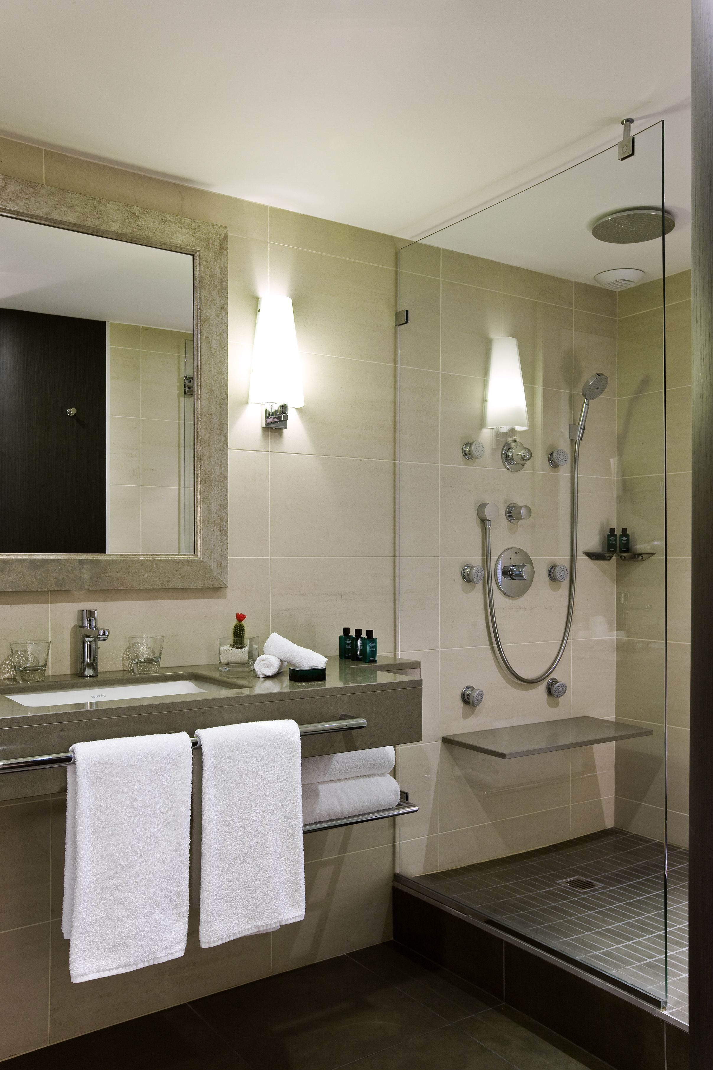 A modern bathroom with a large mirror, dual sinks, a glass shower enclosure, and a towel rack.