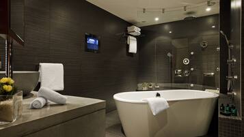 A modern bathroom with a freestanding bathtub, a glass shower enclosure, and a flat-screen TV mounted on the wall.