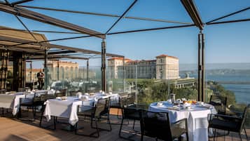 An outdoor dining area with tables set for two, overlooking a body of water and a historic building.