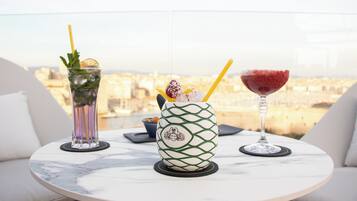 Una mesa con tres bebidas en un balcón con vistas a un paisaje urbano.