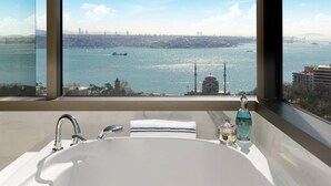 A bathroom with a large window offering a view of a city skyline and a body of water.
