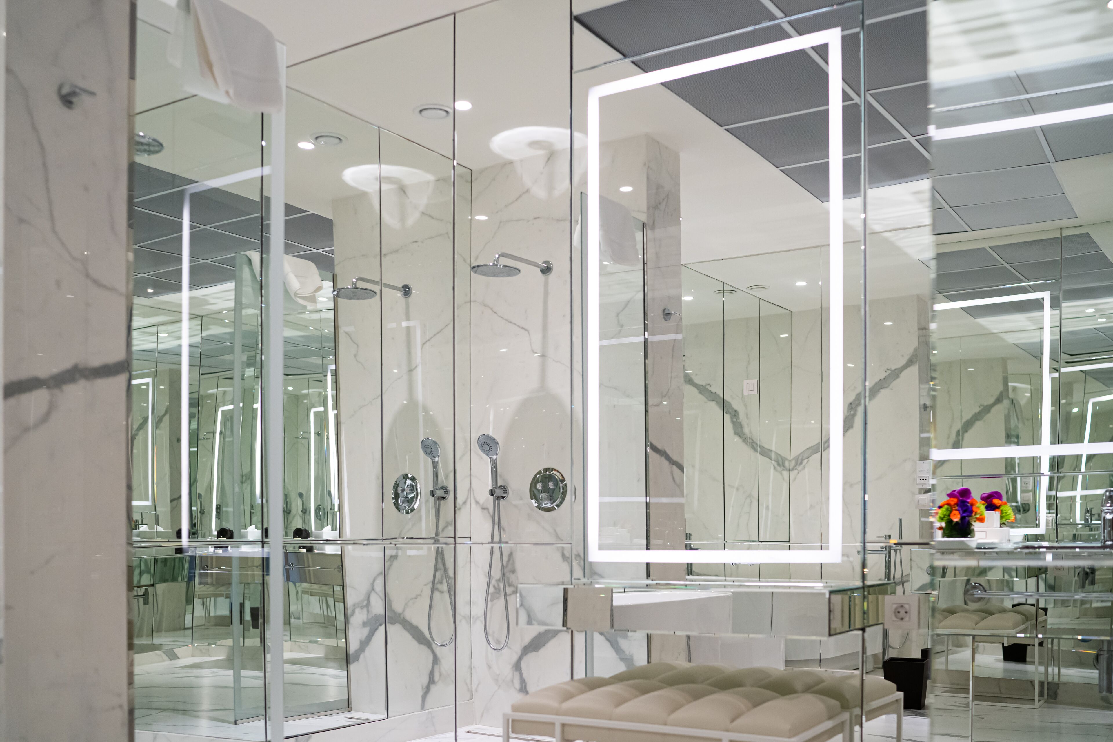 A modern bathroom with a glass shower enclosure, marble walls, and a large mirror.