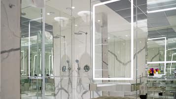 Un baño moderno con cabina de ducha de vidrio, paredes de mármol y un espejo grande.