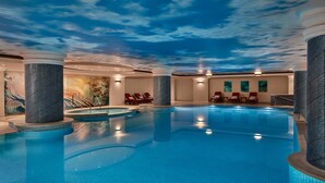 An indoor swimming pool with a ceiling mural, lounge chairs, and a tiled floor.