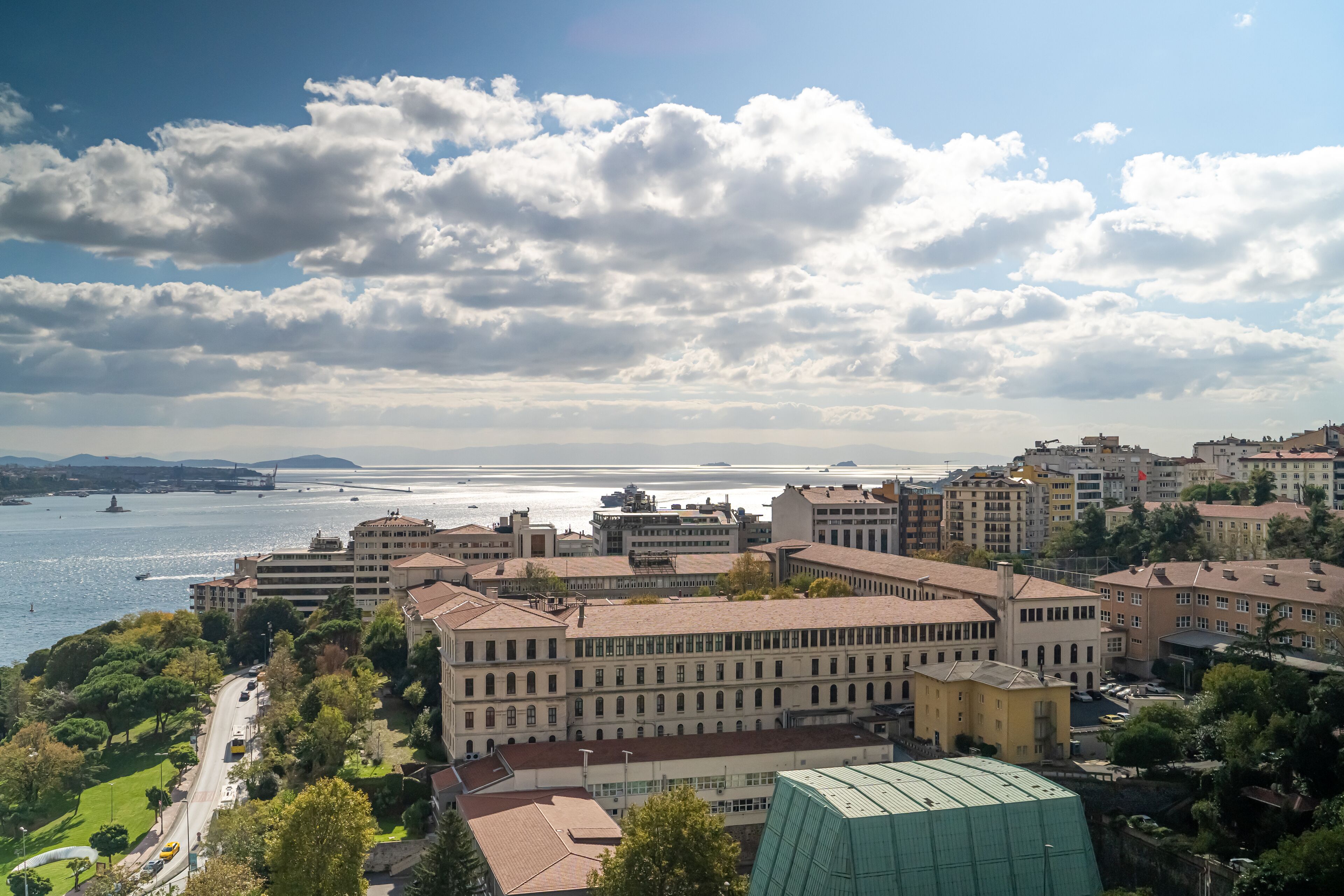 A coastal cityscape with a prominent building complex, a waterfront, and a clear sky.