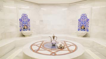 A circular marble-tiled area with a decorative fountain, two wall-mounted sinks, and a central seating area with a patterned floor.