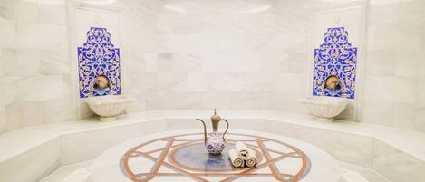 A circular marble-tiled area with a decorative fountain, two wall-mounted sinks, and a central seating area with a patterned floor.