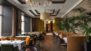 A restaurant with tables set for dining, a chandelier, and potted plants.