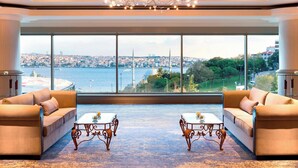 A spacious room with large windows offering a city view, two sofas, and ornate coffee tables.